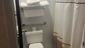 A bathroom with a toilet, a towel rack with folded towels, a shower curtain, and a toilet paper holder.