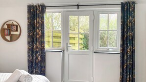 Ein Schlafzimmer mit einem Bett, einem Fenster mit Vorhängen, einer Tür und einem kleinen runden Spiegel mit Büchern.