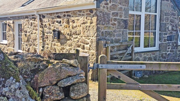 Ein Steinhaus mit schrägem Dach, einem Holztor und einem kleinen Briefkasten.