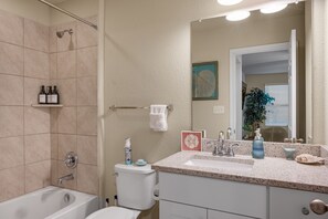 Une salle de bain équipée d’une baignoire, de toilettes, d’un lavabo et d’une douche. On y trouve des articles de toilette sur le lavabo et un porte-serviettes.