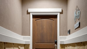 Une porte en bois avec un cadre blanc, un paillasson et une enseigne fixée au mur.