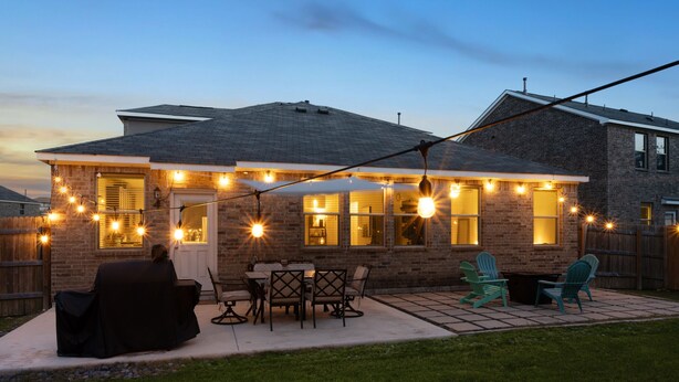 Une maison en briques avec un patio, des sièges d’extérieur et des guirlandes lumineuses.