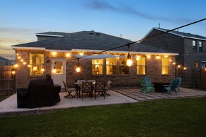 Une maison en briques avec un patio, des sièges d’extérieur et des guirlandes lumineuses.