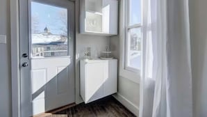 Ett rum med en vit dörr, ett fönster med utsikt över en byggnad och ett vitt skåp med en spegel.