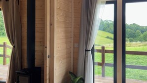 A wooden cabin with a large window, curtains, and a view of a green landscape. - Primrose (Chard)