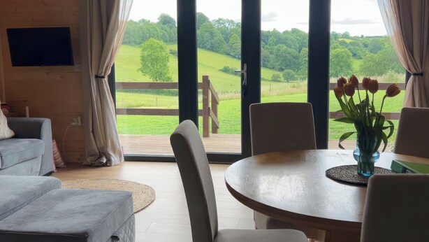 A cozy room with a large sliding glass door leading to a deck, a round dining table with chairs, and a comfortable sofa. - Primrose (Chard)