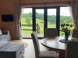 A cozy room with a large sliding glass door leading to a deck, a round dining table with chairs, and a comfortable sofa.