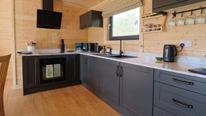 A modern kitchen with wooden walls, a built-in oven, a microwave, a sink, and a coffee maker. - Primrose (Chard)