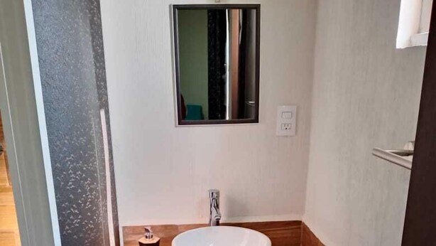 A bathroom with a white sink, wooden countertop, and a mirror above it.