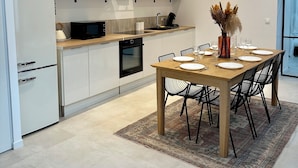 Una cucina moderna con mobili bianchi, una cappa aspirante nera e un'area pranzo con tavolo e sedie in legno.