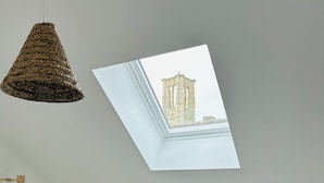 Una stanza con soffitto spiovente, un lucernario, una gruccia di legno, un cesto intrecciato e un pavimento a parquet a spina di pesce.
