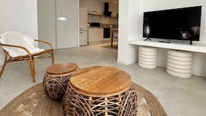 Un soggiorno moderno con mobili in vimini, una TV a schermo piatto e una cucina sullo sfondo.