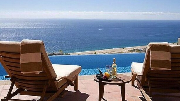 Blick über den Pool mit zwei Liegestühlen und einem Tisch mit einer Flasche und Früchten.