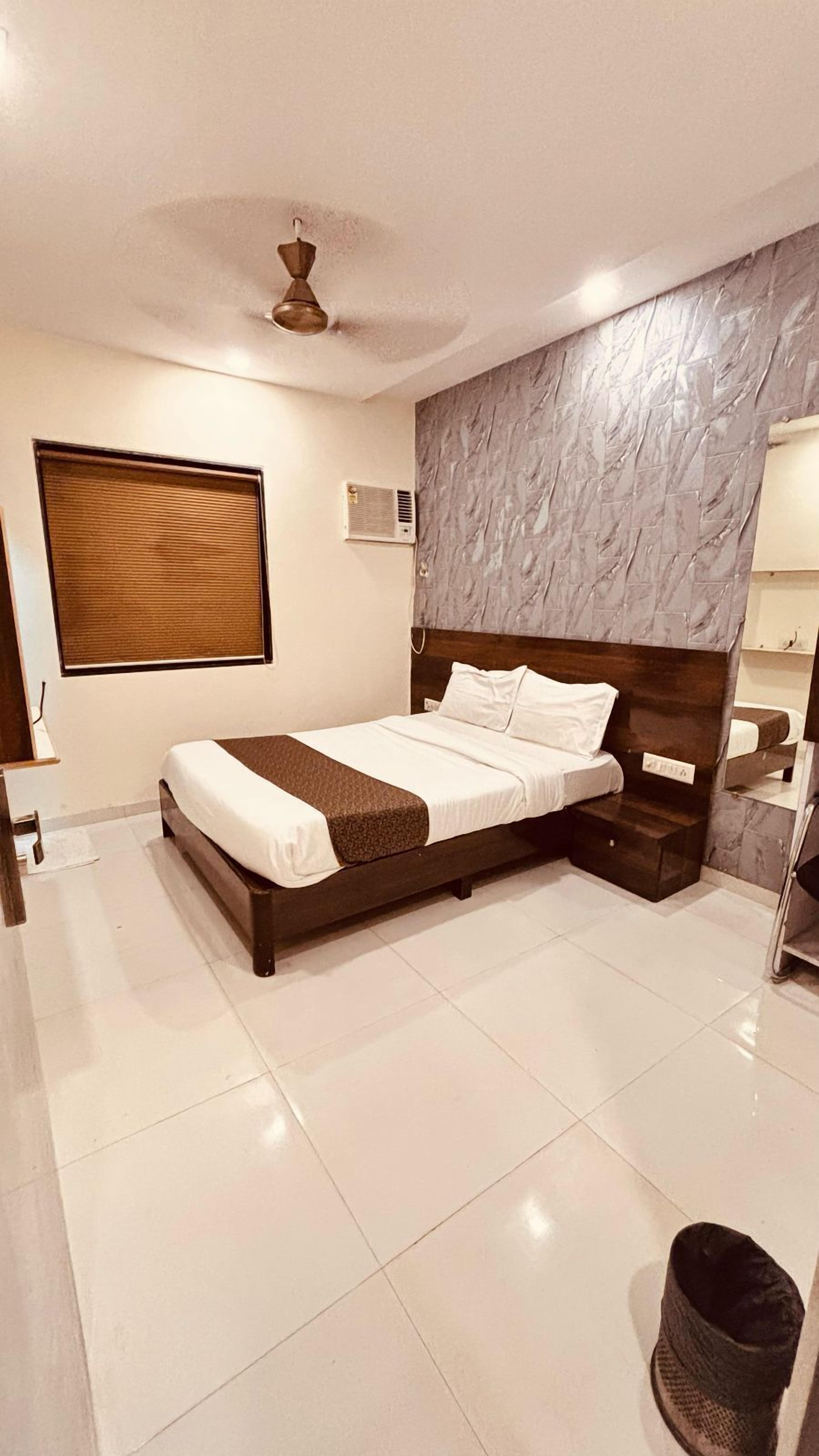 A modern bedroom with a large bed, a ceiling fan, a window with blinds, and a marble-textured wall.