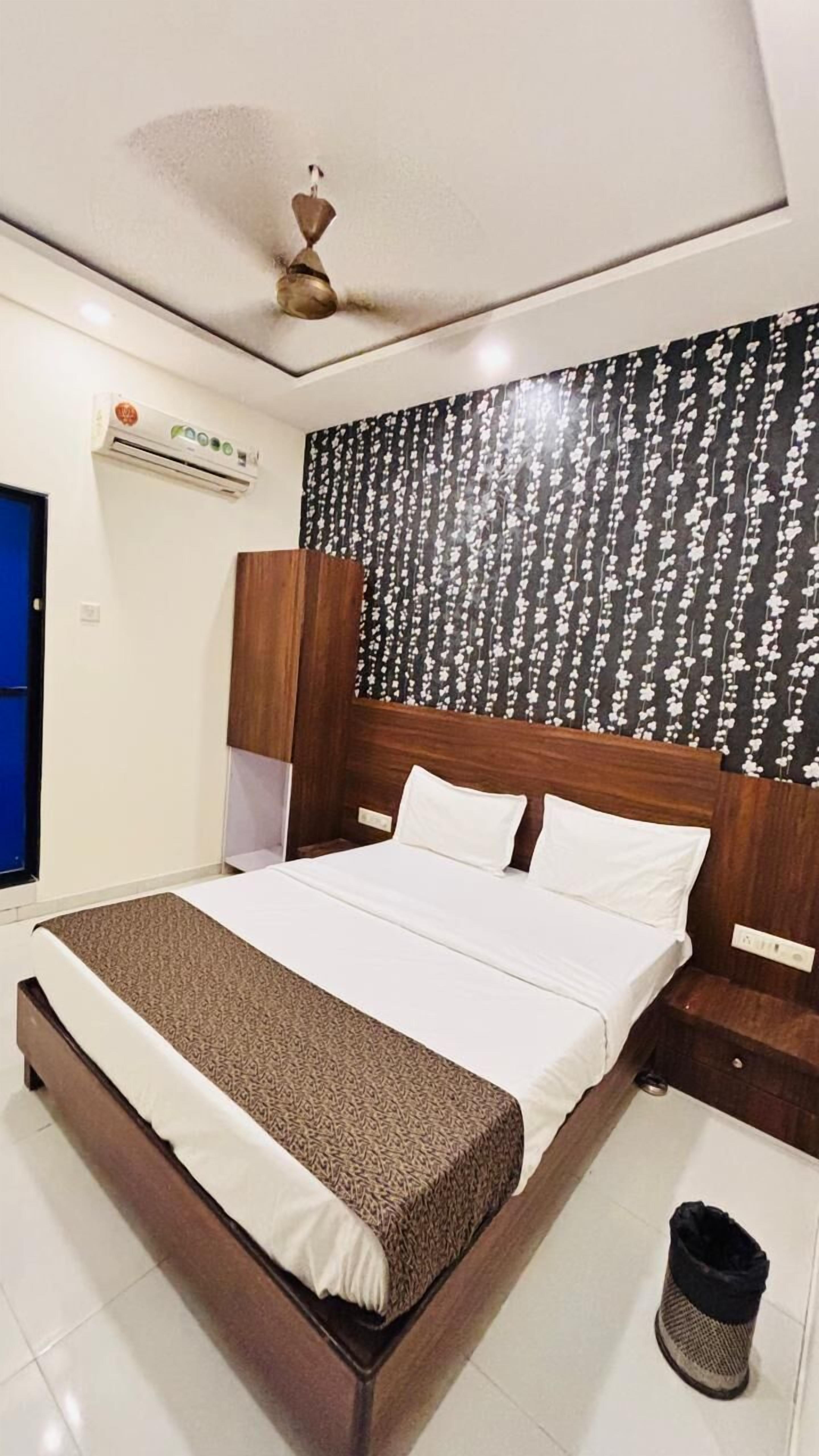 Une chambre d’hôtel avec un lit, une tête de lit en bois, un ventilateur de plafond et un climatiseur mural.
