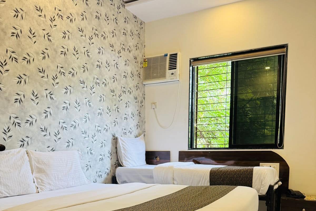 Habitación de hotel con dos camas, ventana con vistas a zonas verdes, pared con estampado de hojas y mesita de noche con teléfono.