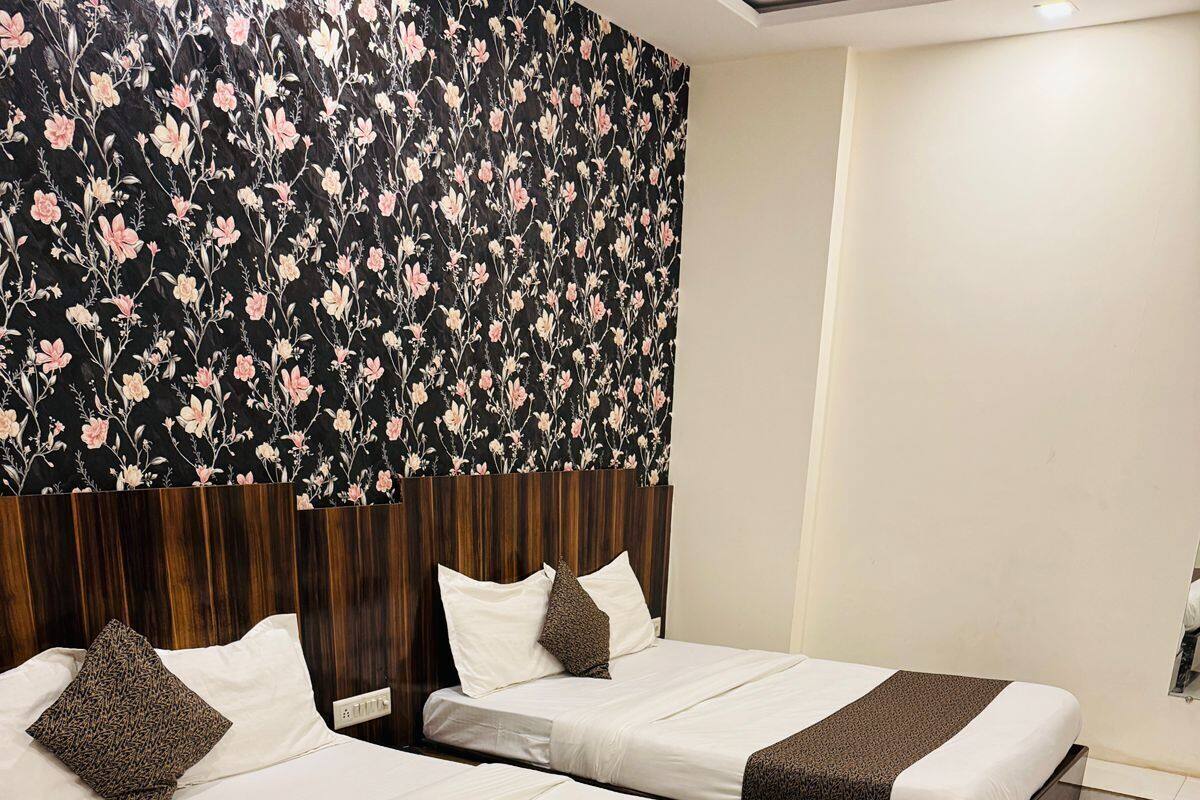 Habitación de hotel con dos camas, cada una con ropa blanca y mantas marrones. La habitación cuenta con un cabecero de madera y un diseño de papel tapiz con motivos florales.