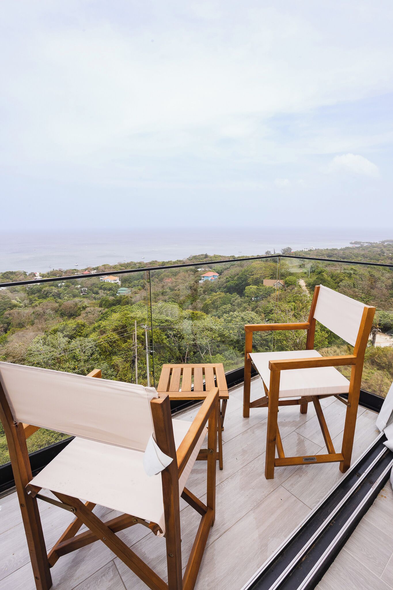 Un balcon avec deux chaises en bois et une petite table, d’où l’on peut admirer un paysage luxuriant et la mer.