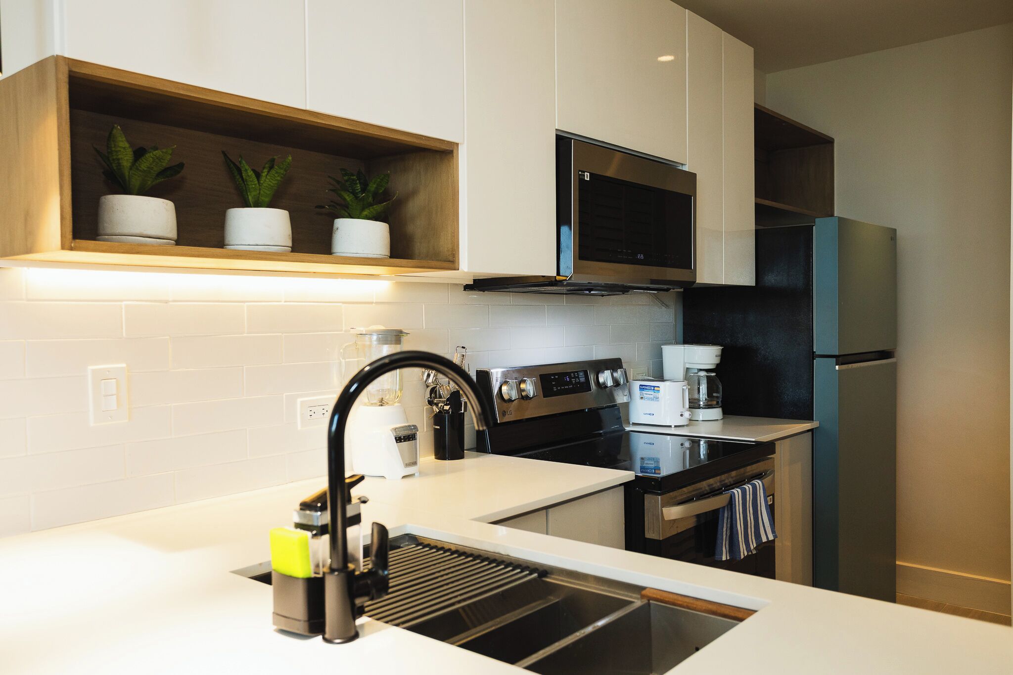 Una cocina moderna con armarios blancos, un lavamanos de acero inoxidable, una campana extractora LG, un microondas y un refrigerador negro.