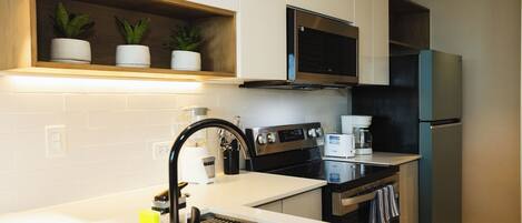 A modern kitchen with white cabinetry, a stainless steel sink, an LG range hood, a microwave, and a black refrigerator.