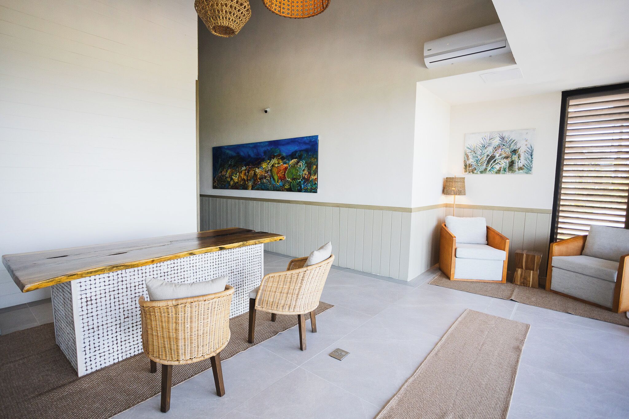 A modern living room with a wooden bar, wicker chairs, and a large abstract painting on the wall.