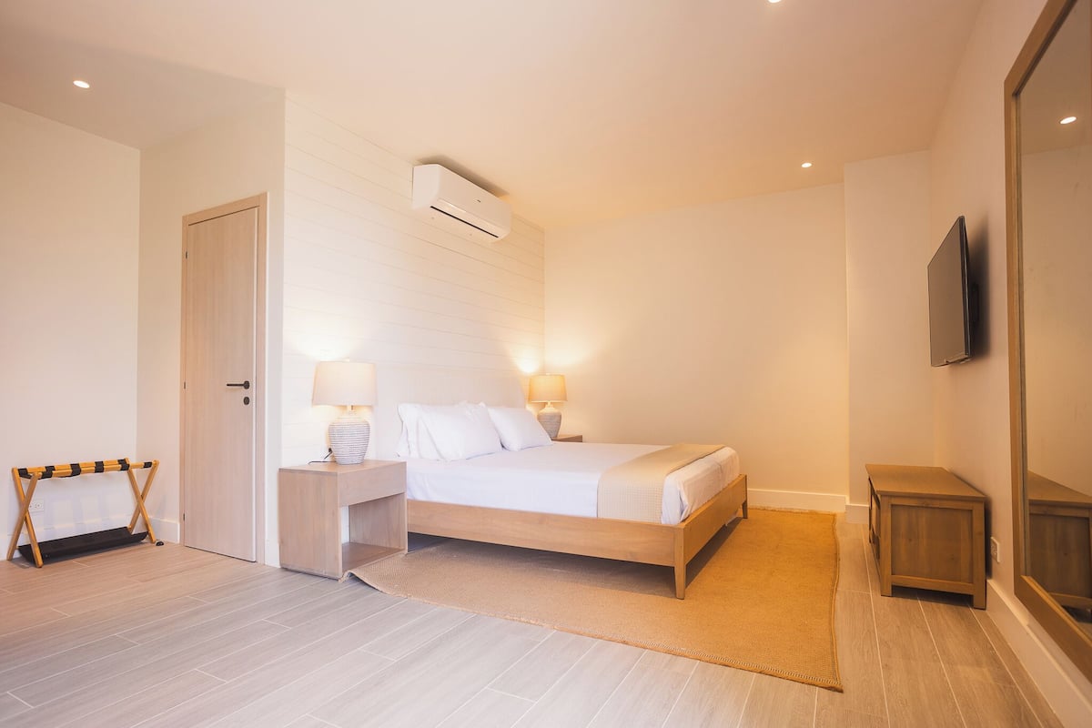 A bedroom with a bed, bedside lamps, a TV, and a wooden floor.