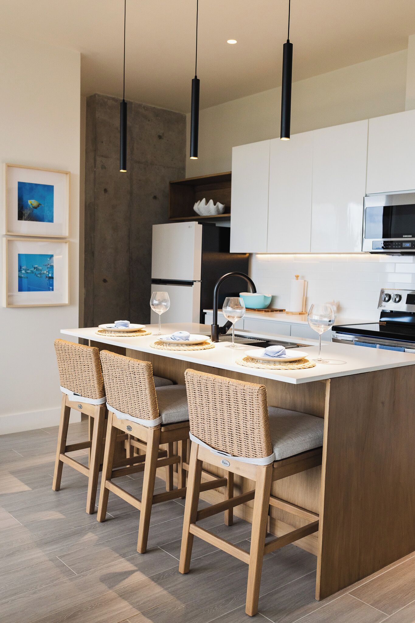 A modern kitchen with a central island, wooden chairs, and pendant lighting.