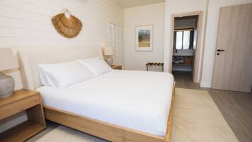 A bedroom with a wooden bed, a bedside table, a hanging wall decoration, a framed picture, and a door leading to another room.