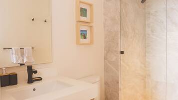 Un baño con lavamanos blanco, inodoro, espejo y cabina de ducha.
