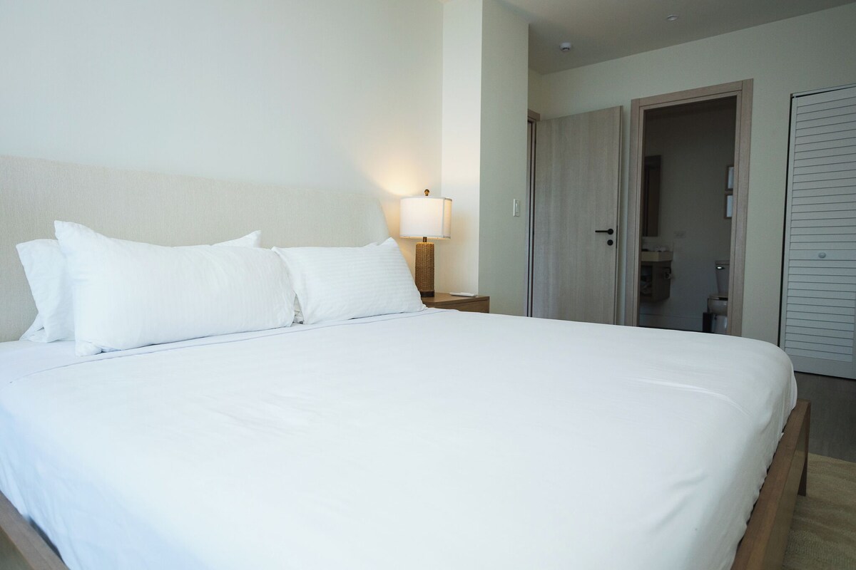 Habitación de hotel con una cama grande, una lámpara de noche y una puerta que da a un baño.