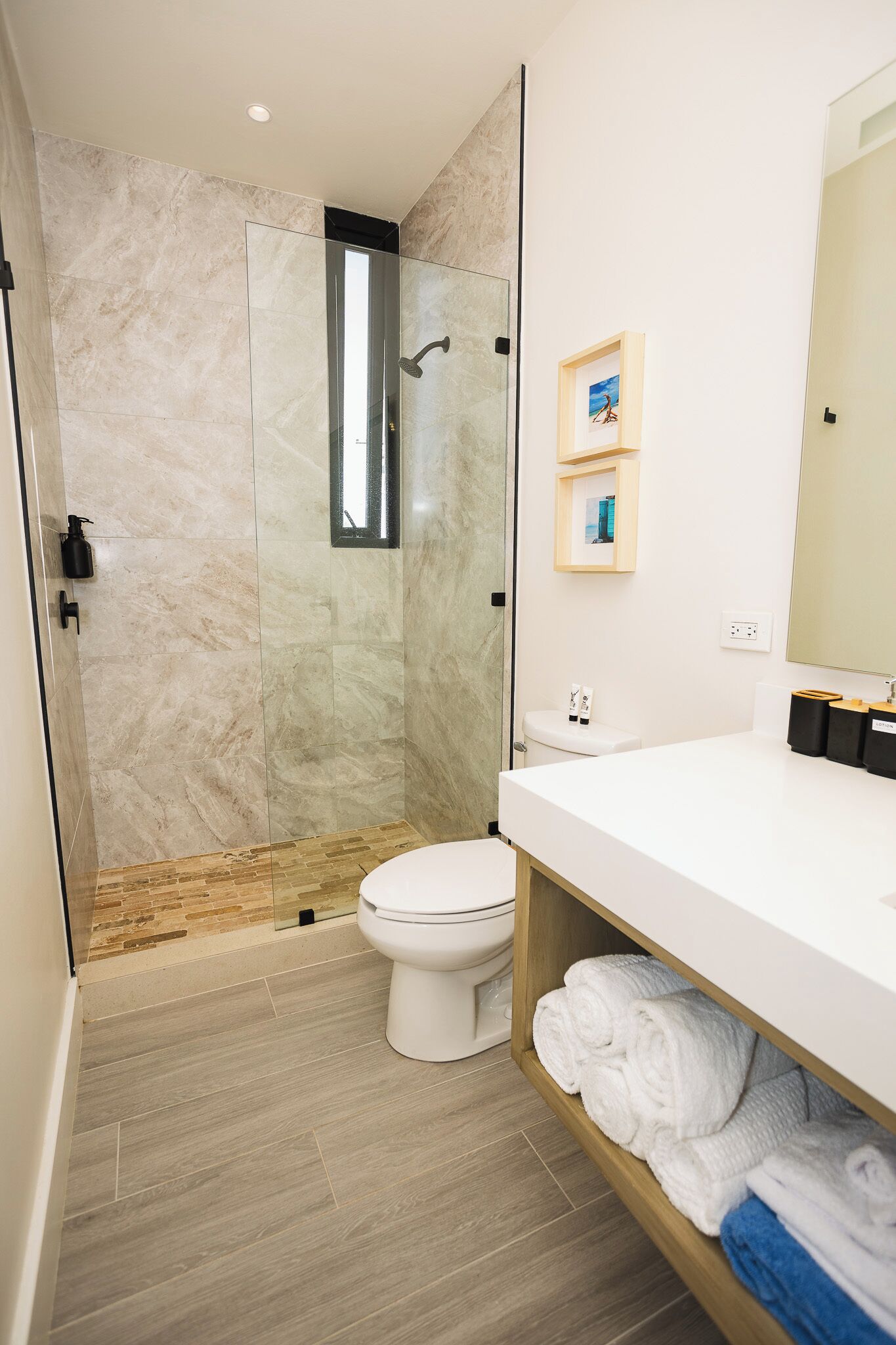Een moderne badkamer met een douchecabine van glas, een wit toilet en een witte wastafel met een houten plank waarop handdoeken liggen.