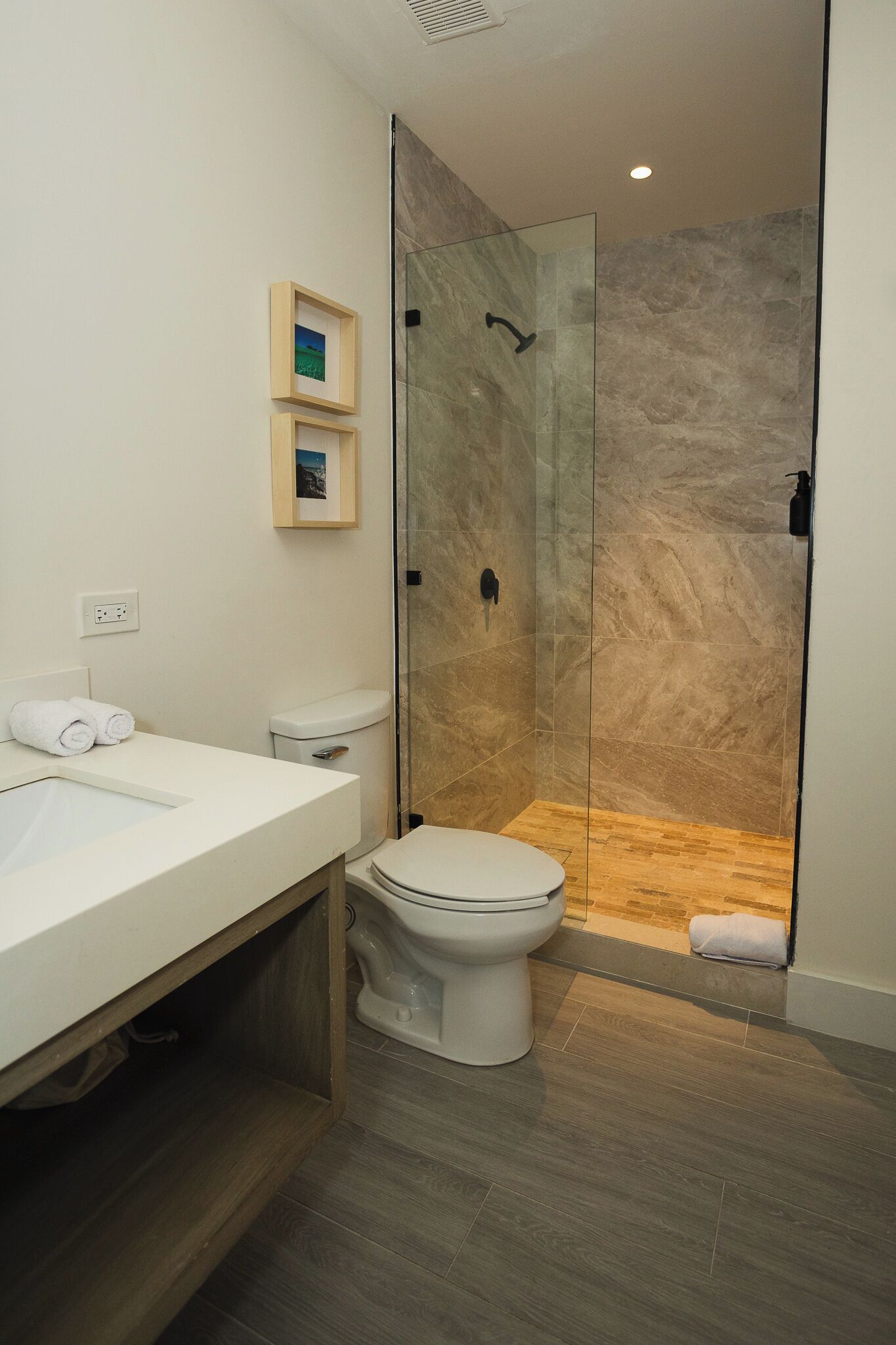 Un baño moderno con ducha de vidrio, inodoro blanco y tocador de madera.