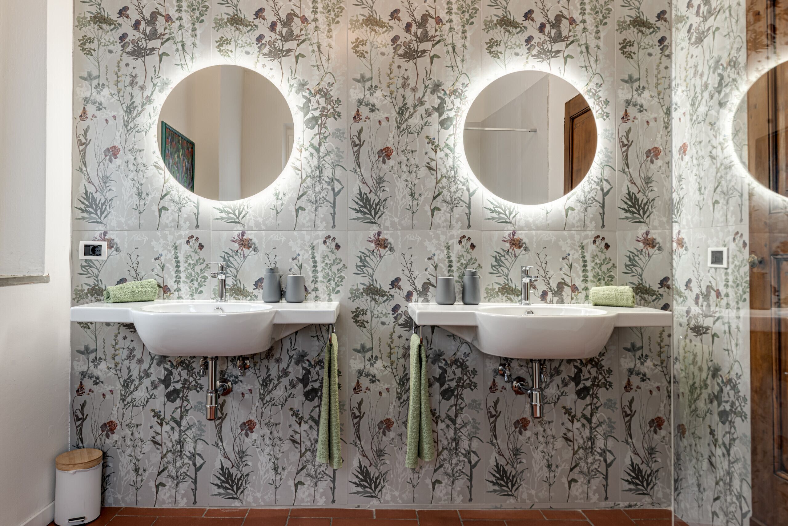 A bathroom with two sinks, two round mirrors, and floral wallpaper.