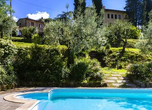 Ein Pool mit Steinbord, umgeben von üppigem Grün und einem Steinhaus im Hintergrund.