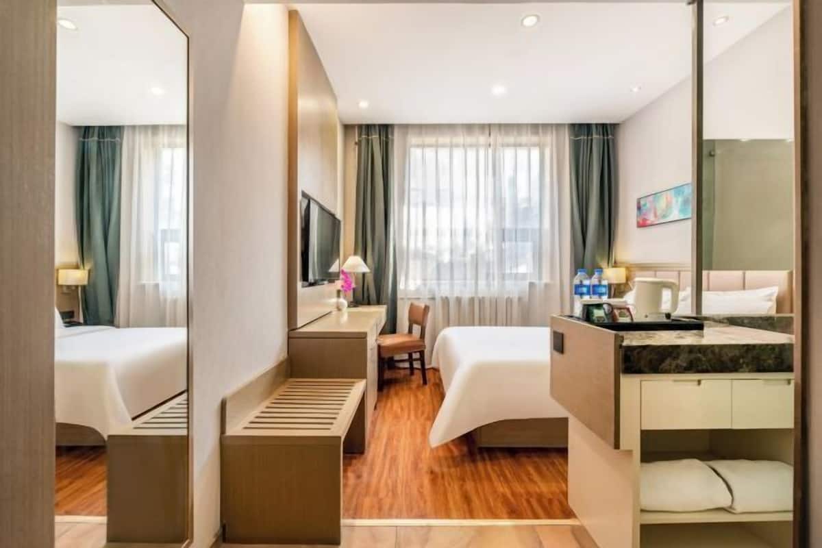 A hotel room with two beds, a desk, a chair, a TV, and a bathroom with a shower curtain.