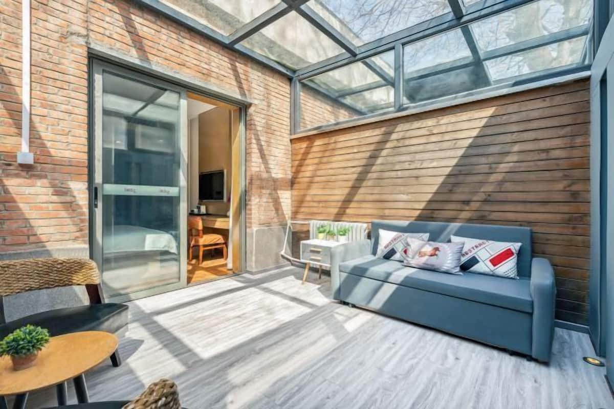 A modern interior with a glass door leading to a room, a blue sofa, a small table with a plant, and a wooden wall.