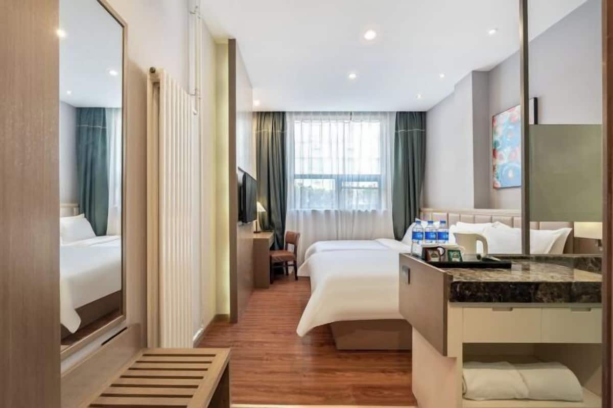 A hotel room with a bed, a desk, a chair, a mirror, and a window.