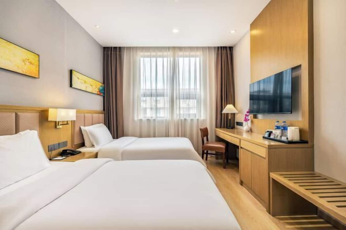 A hotel room with two beds, a desk, a chair, a TV, and a window with curtains.