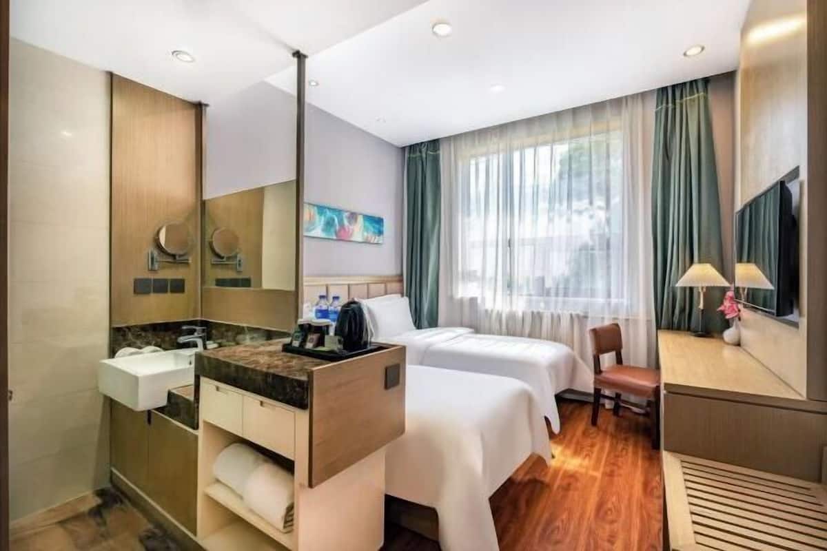A hotel room with a bed, a desk, a chair, a bathroom with a sink and mirror, and a window with curtains.