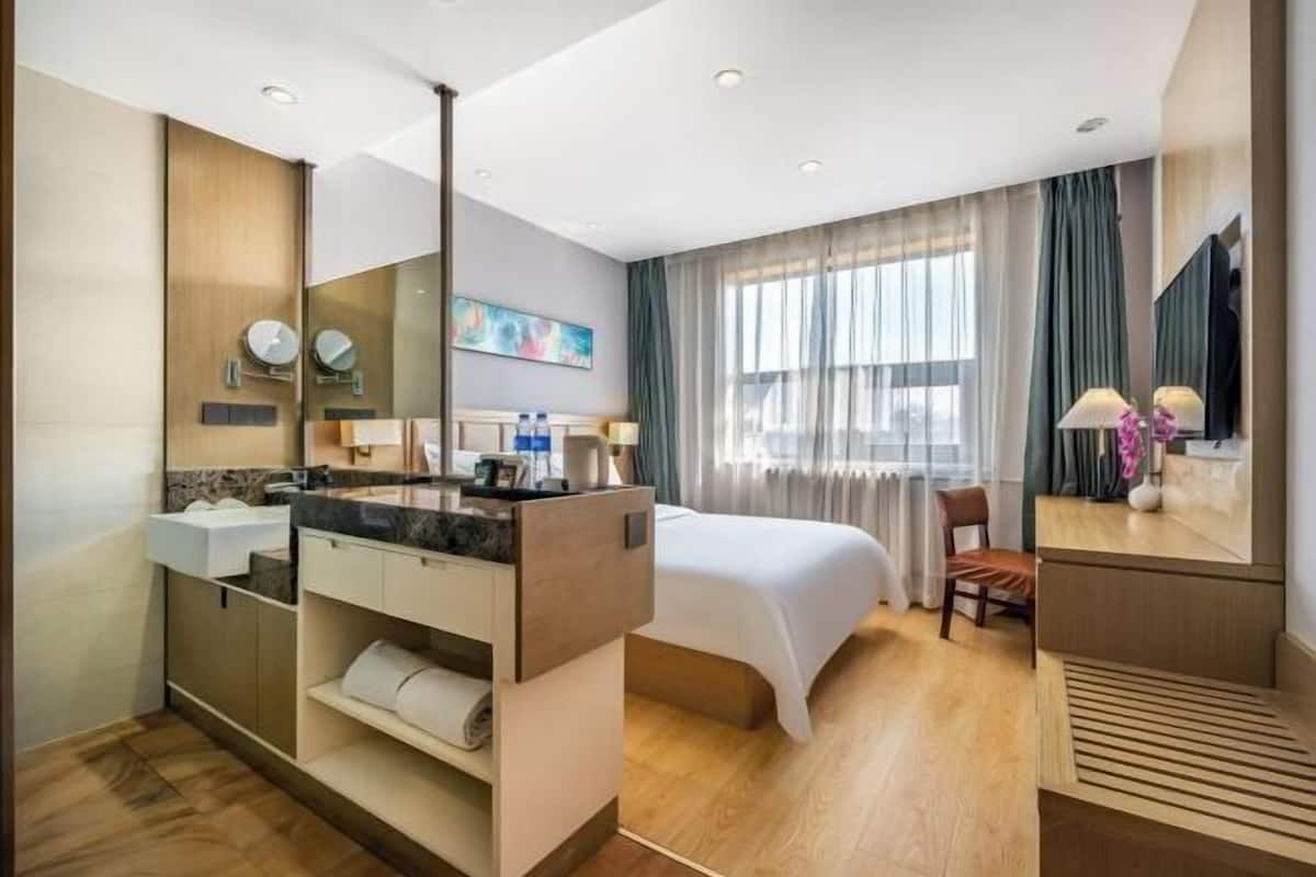 A modern hotel room with a large bed, a bathroom with a vanity, and a large window with curtains.