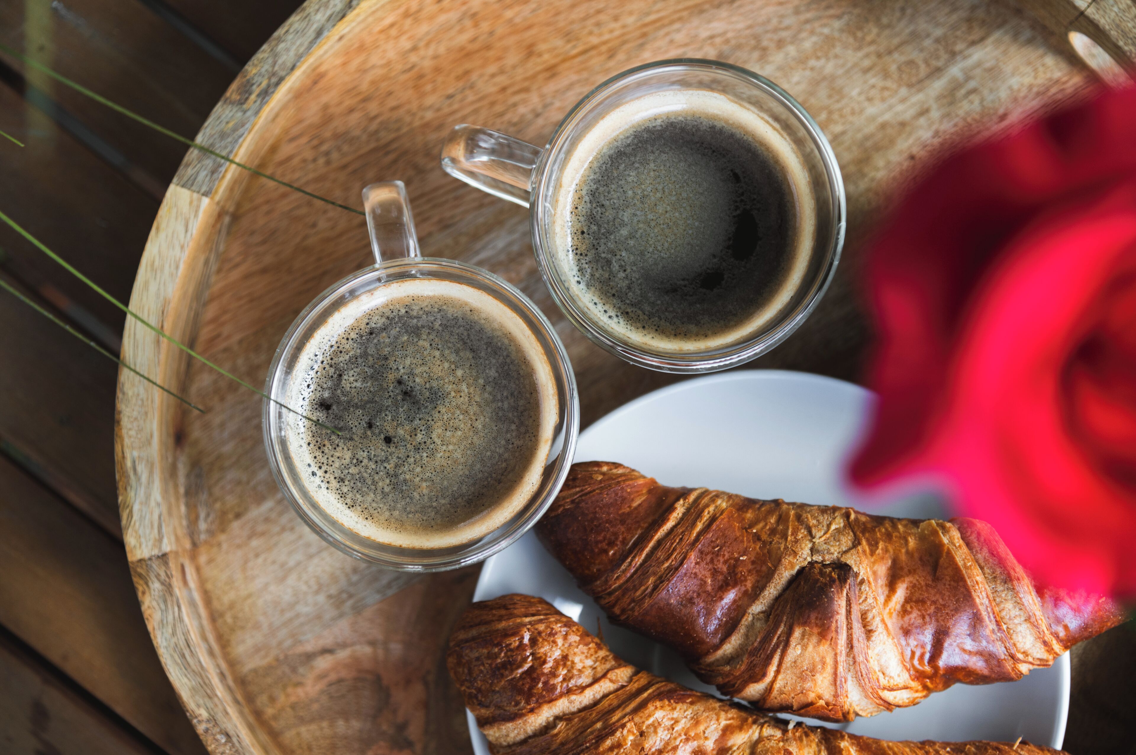 Two clear mugs of coffee on a wooden tray with croissants.