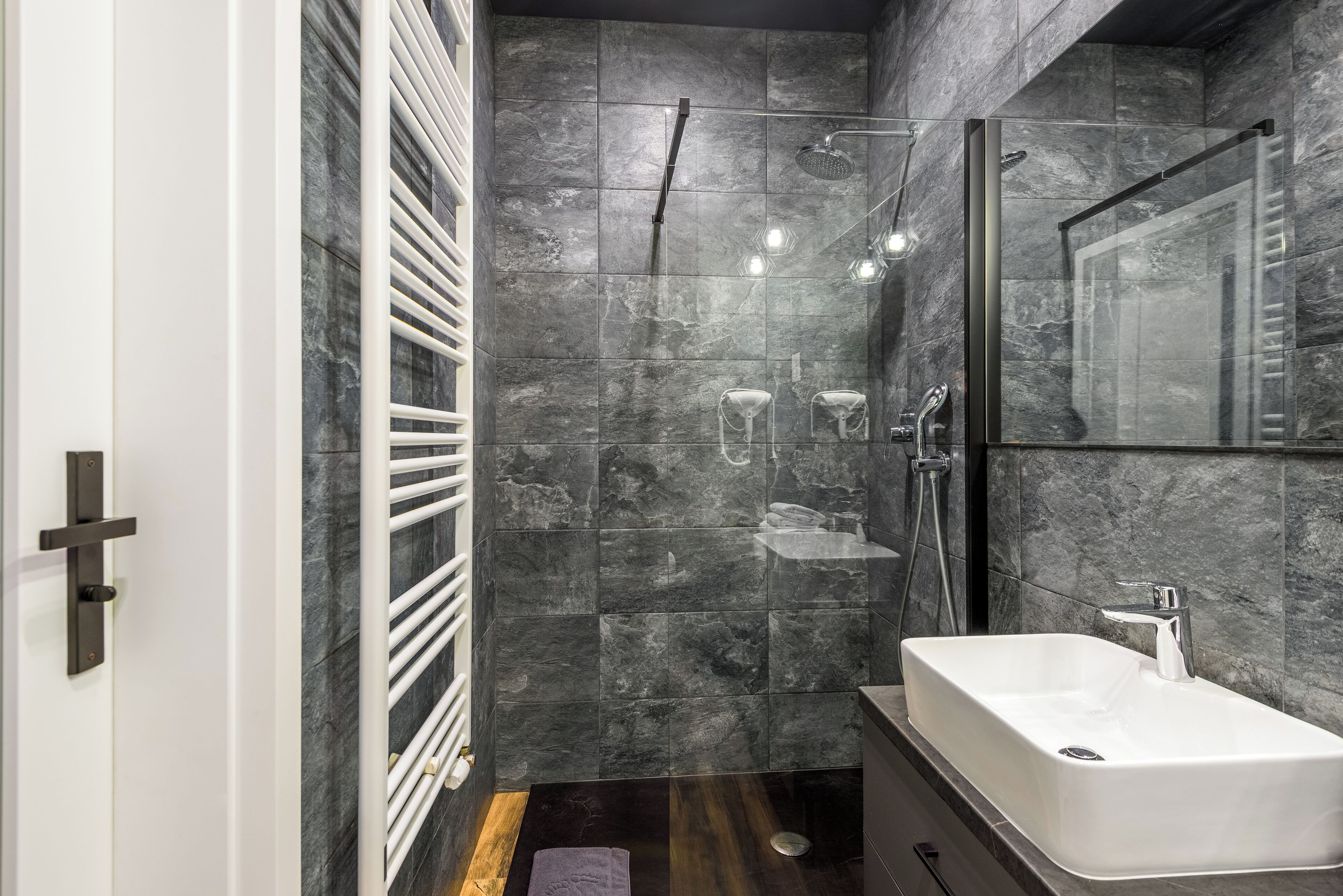 Ein modernes Badezimmer mit einem großen rechteckigen Waschbecken, einer Duschkabine aus Glas und einer Wand mit Marmorfliesen.