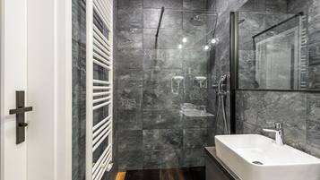 Ein modernes Badezimmer mit einem großen rechteckigen Waschbecken, einer Duschkabine aus Glas und einer Wand mit Marmorfliesen.
