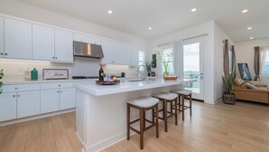 Una cocina moderna con gabinetes blancos, una campana extractora de acero inoxidable y una isla central con taburetes.