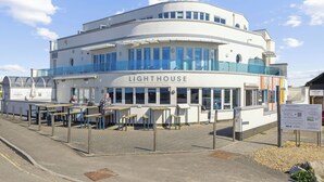 A white building with a curved facade, labeled "LIGHTHOUSE," featuring outdoor seating and a glass railing. - Blue Horizon (Lymington)