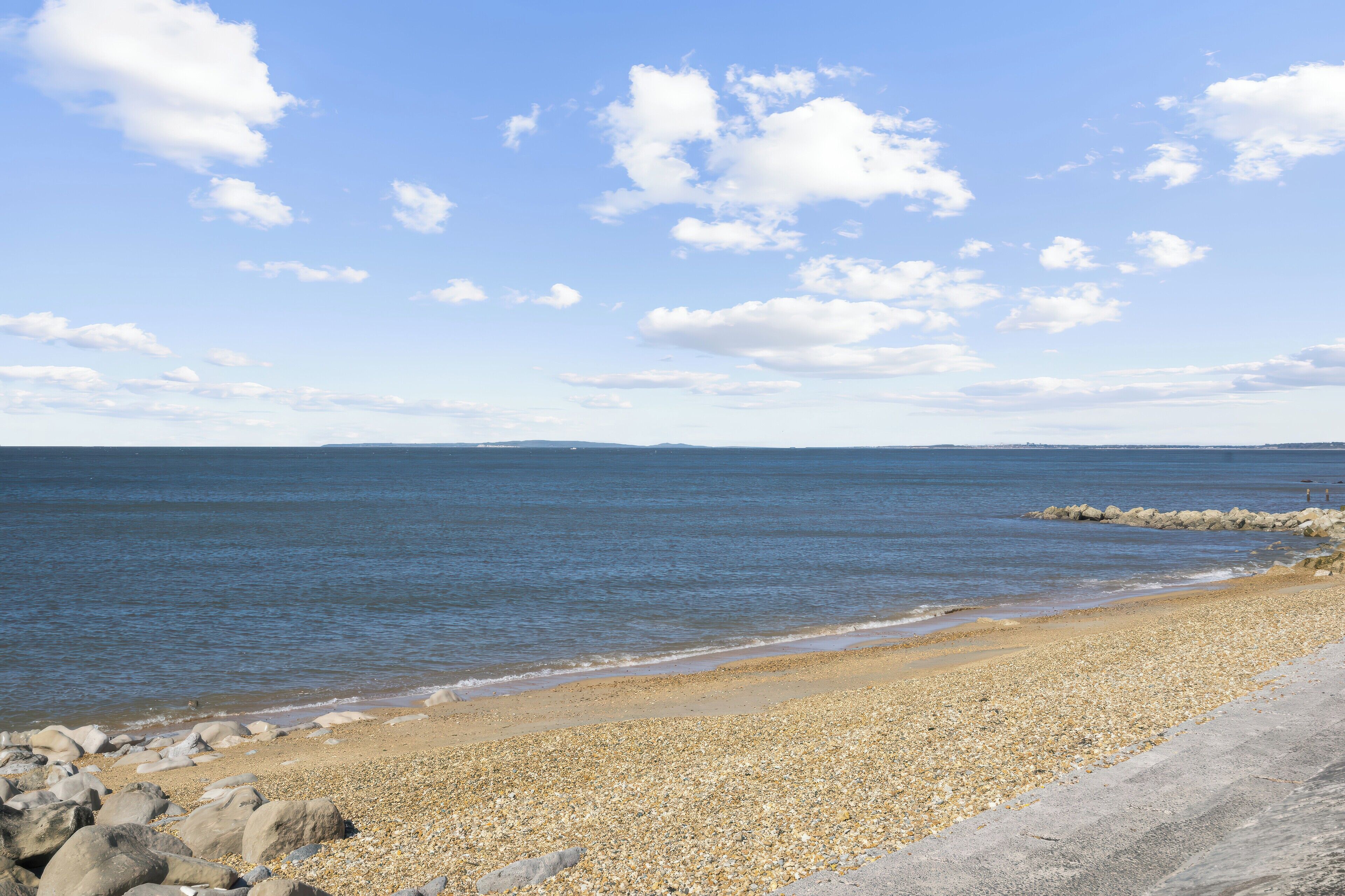 A pebble beach with a rocky shoreline and calm sea under a clear sky.
