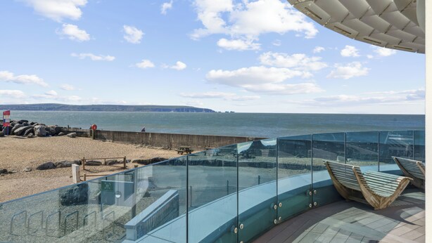 A glass balustrade overlooking a beach with a view of the sea and distant cliffs. - Blue Horizon (Lymington)