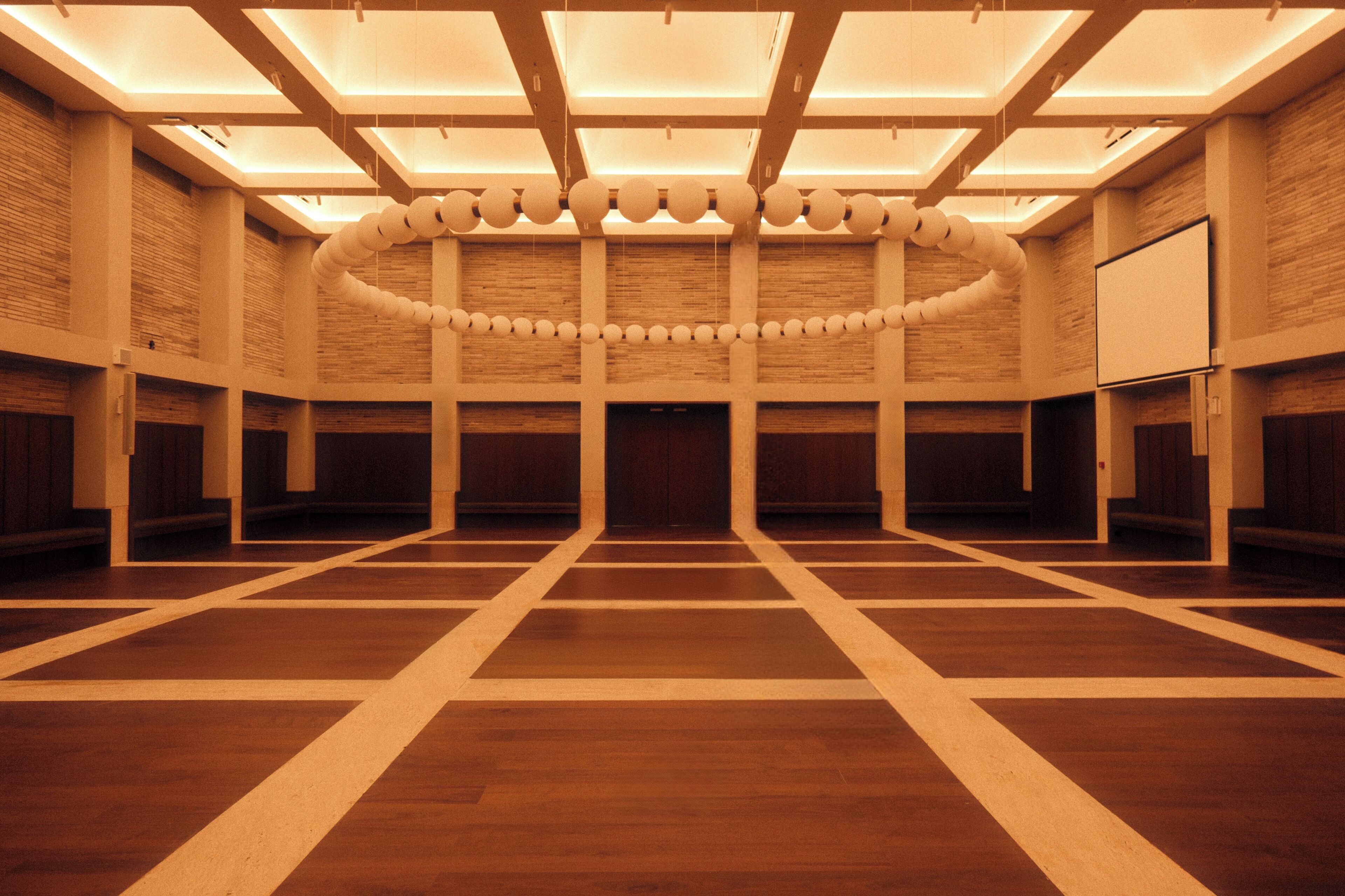 Un amplio salón con techo alto, paneles de madera y una disposición circular central de objetos esféricos.