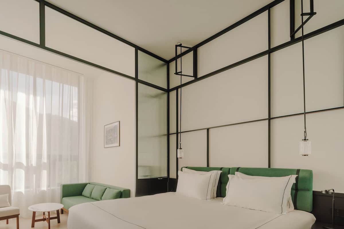 A modern bedroom with a large bed, a green sofa, a small table, and a nightstand.