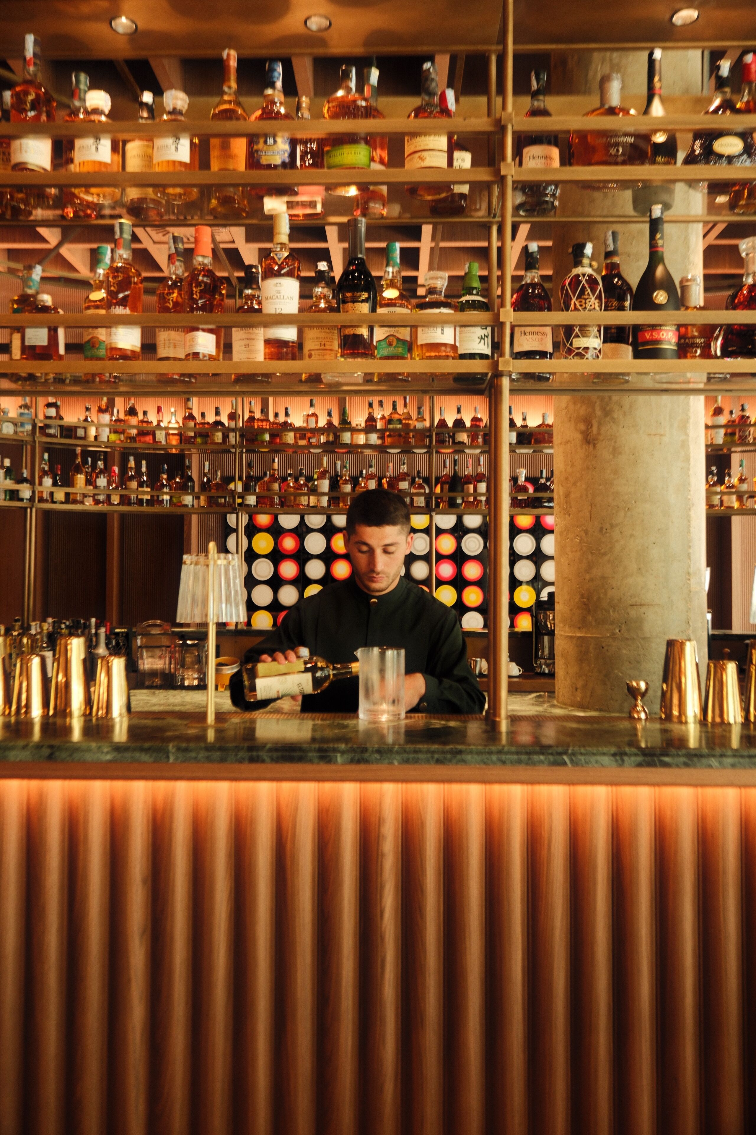 Un bar con estantes llenos de botellas de licor y un bartender preparando bebidas.